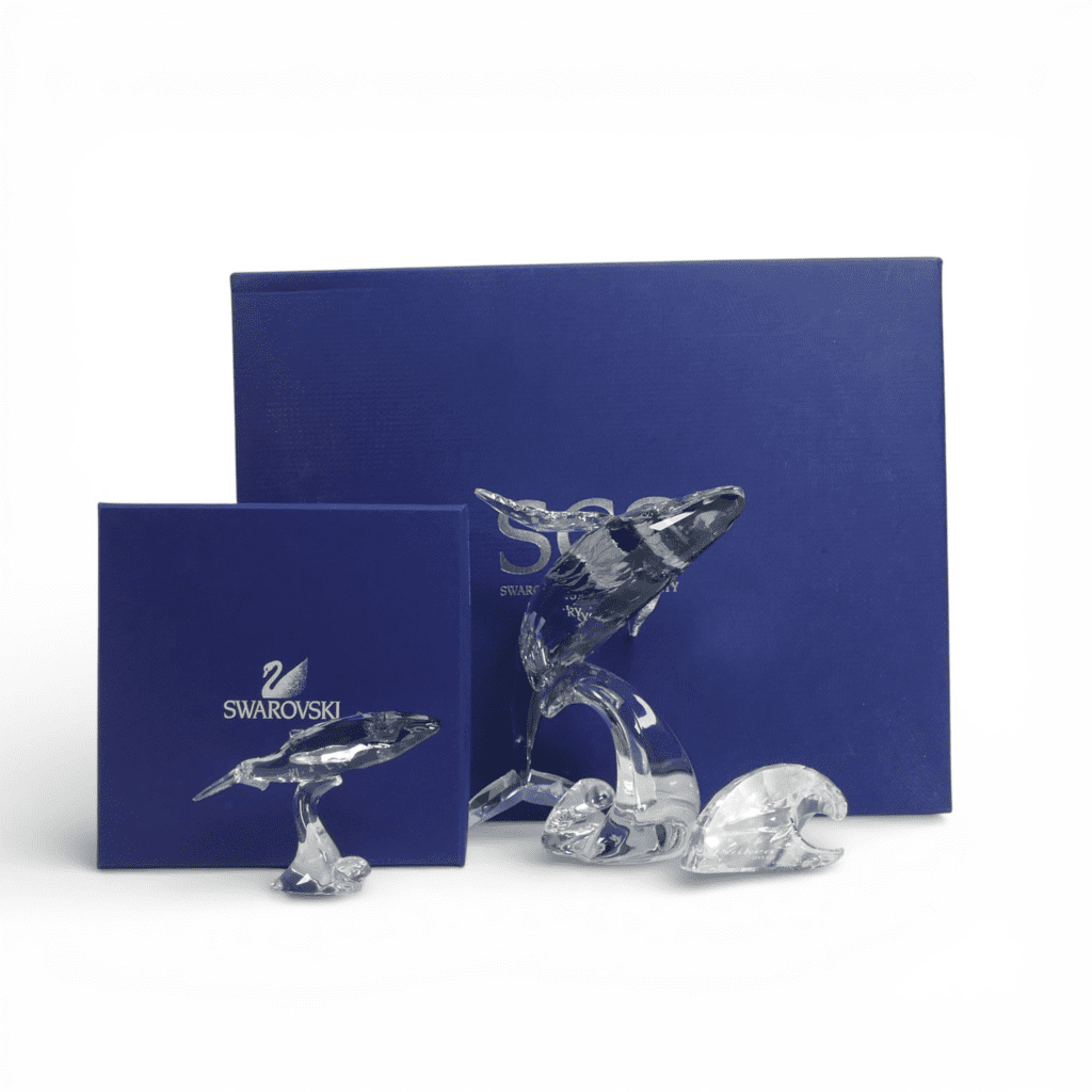 Swarovski Paikea Humpbacked Whale with Wave Plaque (1095228) together with Young humpbacked Whale (1096741) both retired 2012 designed by Stefanie Nederegger presented in shadow crystal with moonlight fins. Tallest:-16cm. Boxed with certificate of authenticity (3)