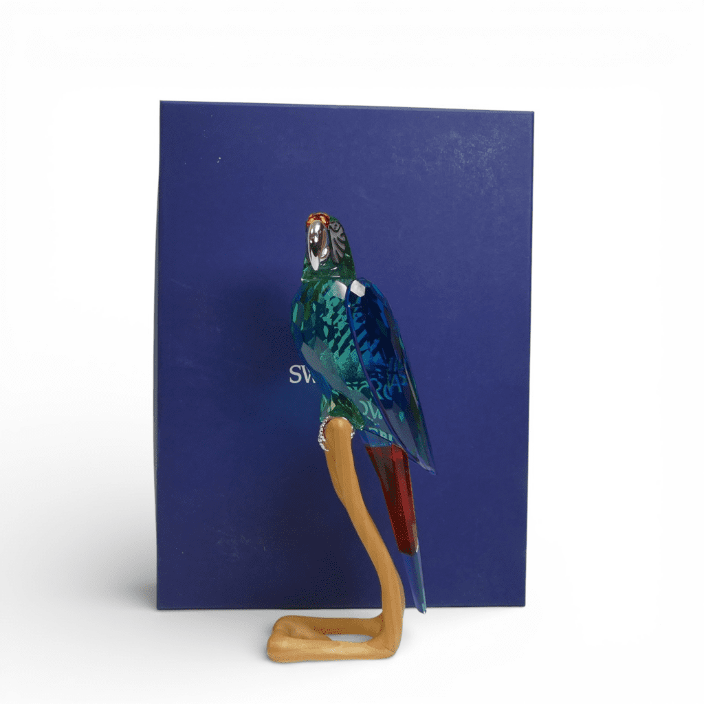 Swarovski Crystal Paradise Macaw (chrome green), mounted on wooden perch, by Roland Schuster, with original box and certificate (685824) retired 2011. (H: 24.5cm)