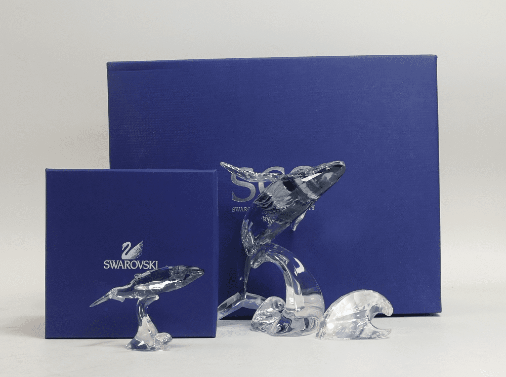 Swarovski Paikea Humpbacked Whale with Wave Plaque (1095228) together with Young humpbacked Whale (1096741) both retired 2012 designed by Stefanie Nederegger presented in shadow crystal with moonlight fins. Tallest:-16cm. Boxed with certificate of authenticity (3)