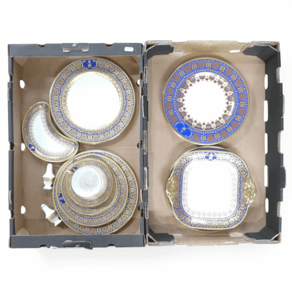 De Lamerie Fine Bone China, a collection of tea and dinner ware with heavy gilt decoration, made specially for His Majesty The Sultan of Oman, to include - plates, square serving plate, tea cup, saucer, side plates, salt and pepper pots and crescent-shaped plate. Made in England (approx. 17 pieces) (2 Trays)
